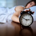 Nő ébren fekszik az ágyban, az előtérben ébresztőóra hajnali 3 órai idővel