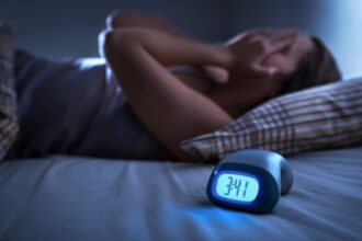 Éjszaka felriadó nő az ágyban, digitális óra 3:41-es idővel